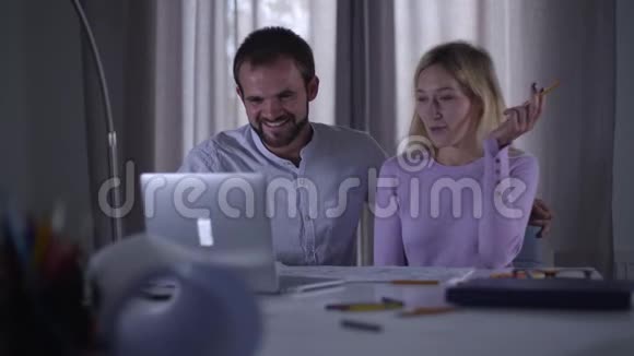 开朗的白人同事在笔记本电脑里看着笑男性和女性专业人士观看搞笑视频或视频的预览图
