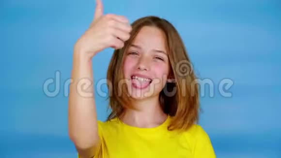 穿着黄色T恤的快乐少女露出舌头竖起大拇指喜欢看镜头视频的预览图