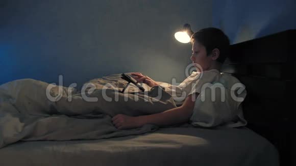 晚上男孩在床上用他的数码平板电脑休息视频的预览图