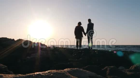 日落时分年轻浪漫夫妇的剪影矗立在海滩上男人握着心爱的女人的手和她说话向我展示视频的预览图
