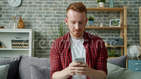 红发胡子男在舒适的公寓里用智能手机发短信视频的预览图