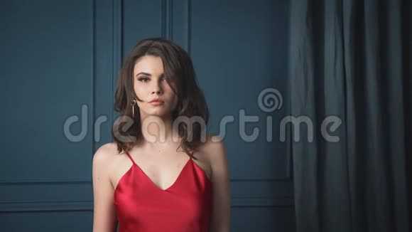美丽的黑发女郎身着丝质红色礼服晚装靠在蓝色的墙壁上晒出奢华的生活魅力视频的预览图