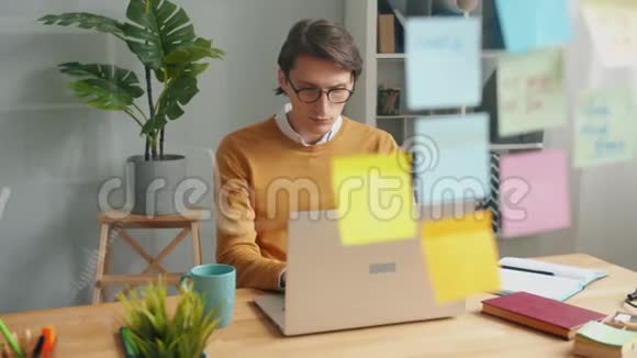 严肃的商人在玻璃墙后面的笔记本电脑上工作上面贴着五颜六色的贴纸视频的预览图