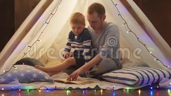 小男孩在家里孩子们的帐篷里玩父亲在读童话快乐的白种人小孩在游戏室视频的预览图