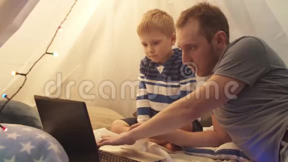 小男孩和他的父亲在家里的儿童帐篷里玩和看动画片快乐的白种人小孩在游戏室视频的预览图