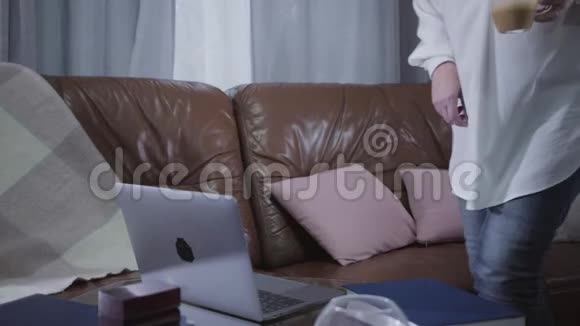 成熟微笑的白种人女人带着卡布西诺来到笔记本电脑和看屏幕资深退休人士上网视频的预览图