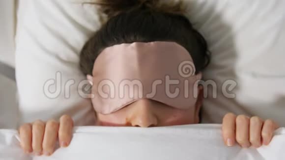 带眼罩的女人躺在毯子下面的床上视频的预览图