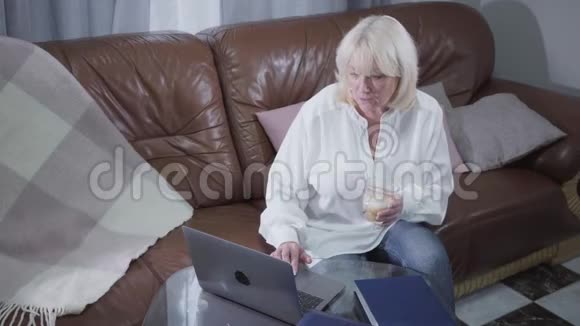 高颜值成熟的白人女性穿着休闲服装喝咖啡和上网高级金发退休人员视频的预览图