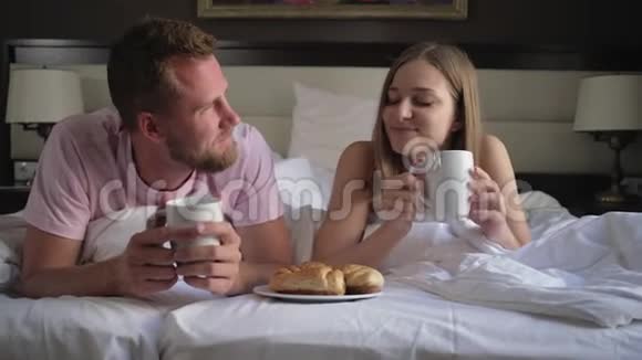 男人和女人早上躺在床上吃羊角面包和咖啡视频的预览图