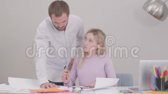 漂亮年轻的高加索女人绘制蓝图她的男同事拿着铅笔帮助她完成这个项目视频的预览图