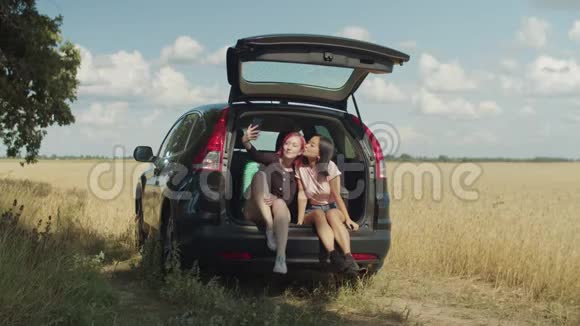 快乐的女性朋友在汽车后备箱里自拍视频的预览图