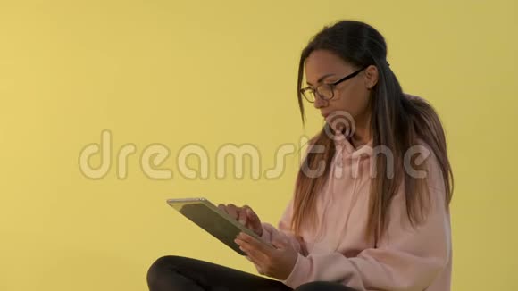 戴眼镜的黑人妇女在黄色背景下制作平板电脑视频的预览图