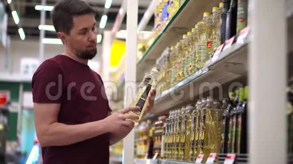 男士购物者在超市的食品过道里拿着带有葵花籽油的瓶子视频的预览图
