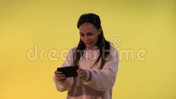 可爱的黑人女孩在黄色背景的智能手机上玩游戏视频的预览图