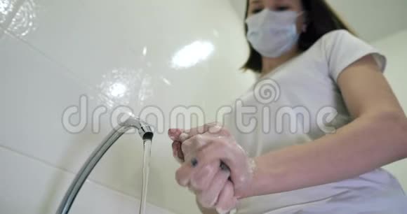 一个戴着医用口罩的女孩洗手以保护她免受感染流行COVID19视频的预览图