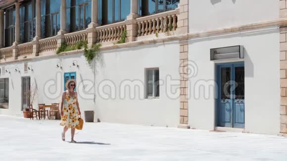 年轻的黑发女人穿着向日葵和黄色手提包走在历史和度假胜地的空街上视频的预览图