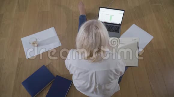 高加索族女性退休人员穿着休闲服装坐在木地板上使用笔记本电脑智能女性视频的预览图