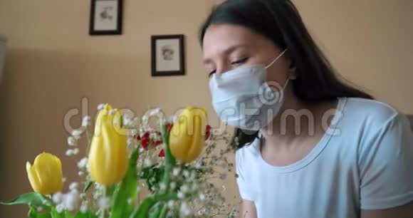 戴着医用面具的年轻女孩闻着花大流行病毒19自我隔离视频的预览图