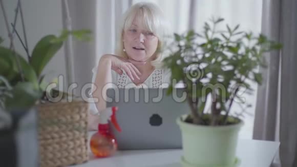 一幅有思想的高高级妇女坐在家里拿着笔记本电脑看着她的园艺作品的肖像成熟女性视频的预览图