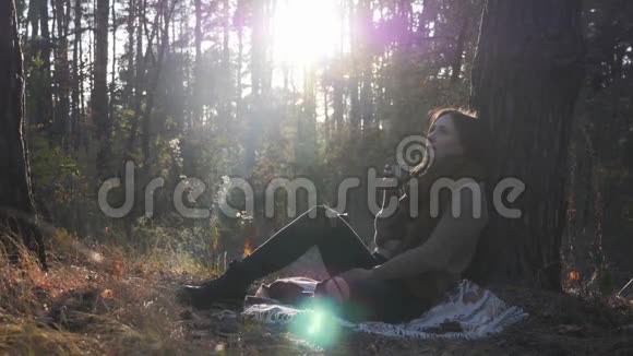 迷人的女旅行者在大自然中喝热茶秋天的森林里阳光明媚年轻美丽的黑发女子在喝咖啡视频的预览图