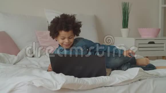 多民族儿童在床上用笔记本电脑键盘打字视频的预览图