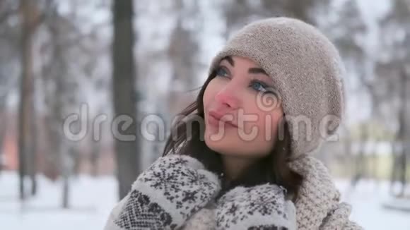 一个戴着帽子和手套的年轻女子在冬季公园里的画像她看向别处微笑着慢动作视频的预览图