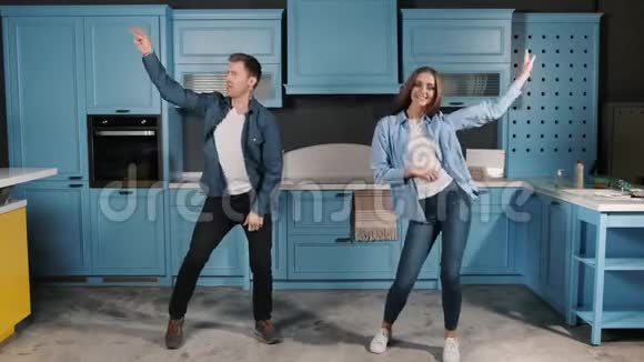 快乐的年轻夫妇在家里的厨房里做饭时玩着跳舞他们微笑着把手臂上下移动视频的预览图