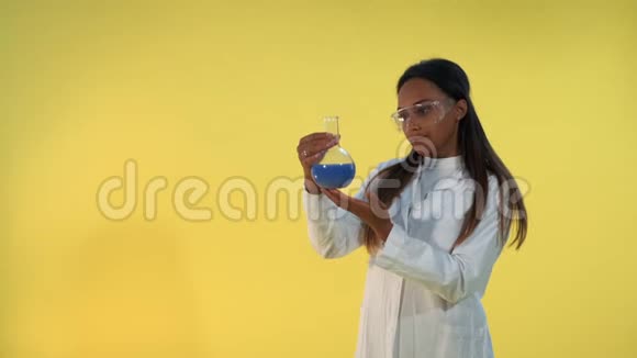 一位身穿实验室工作服的黑人女科学家在黄底的实验液体烧瓶上观看视频的预览图