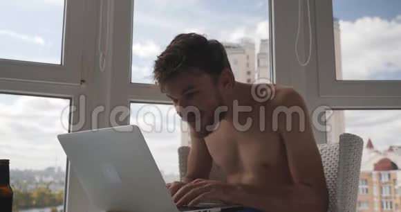 年轻的白种人男商人穿着内裤坐在阳台上手提电脑在金融市场赢得了交易快乐快乐视频的预览图