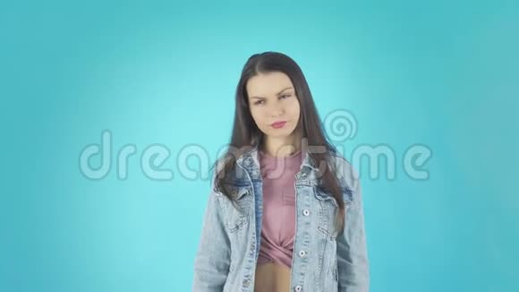 穿着牛仔夹克的年轻疲惫的女人在镜头前对着蓝色的背景视频的预览图