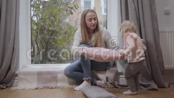 年轻迷人的白人女人坐在低矮的窗台上和小女孩说话穿着粉红色衬衫走路的可爱孩子视频的预览图