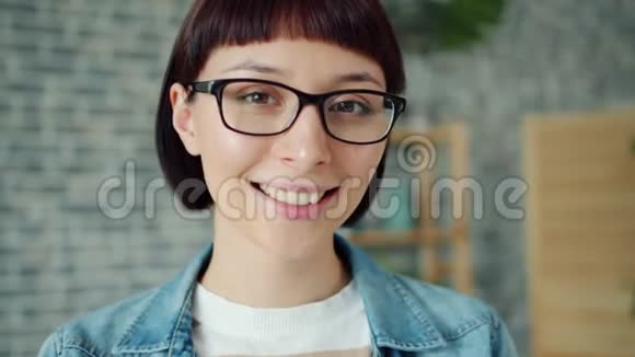 戴着眼镜的年轻漂亮黑发女子独自在家微笑的特写照片视频的预览图