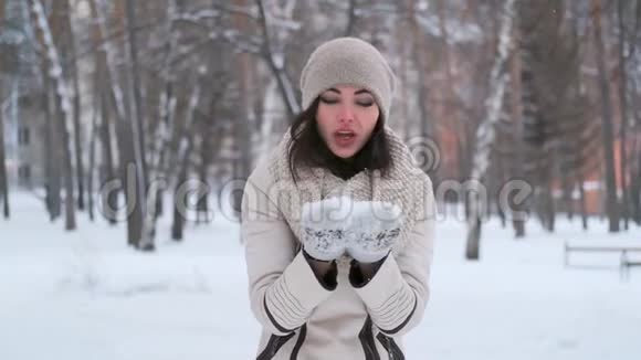 在冬日的森林里一个心情愉快的年轻迷人的女人吹着手套上的雪微笑着慢动作视频的预览图