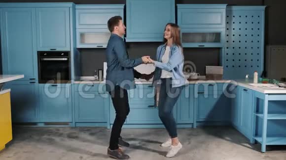 快乐的年轻夫妇在家里的厨房里做饭时玩着跳舞他们牵着手微笑着跳舞视频的预览图