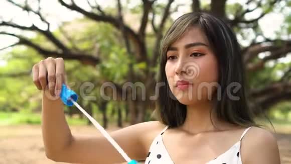 年轻的东南亚20多岁的女人在公园里吹气泡快乐的女孩穿着夏天的裙子和树视频的预览图