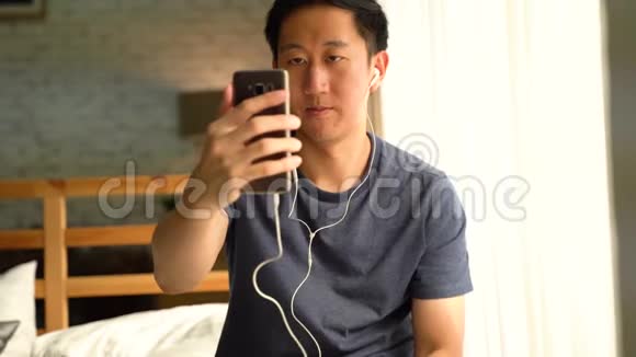 快乐的30多岁亚洲男人的肖像穿着休闲服装面对面的视频通话与智能手机在家里他视频的预览图