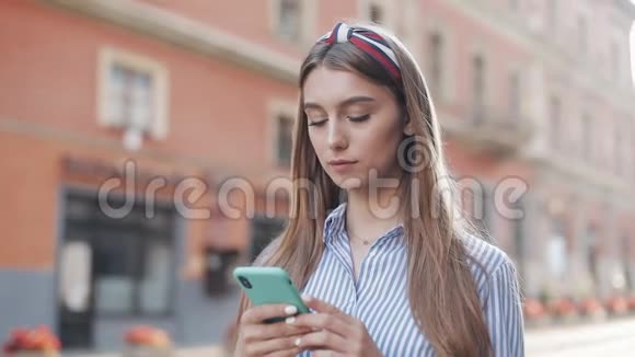 年轻漂亮的棕色头发女孩带着时髦的头巾穿着条纹衬衫拨号电话号码在智能手机和视频的预览图