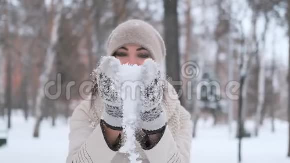 美丽的年轻女子一头乌黑的头发在冬天的公园里拍着手套雪微笑着非常高兴慢动作视频的预览图