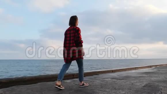 迷人的年轻黑发女性在日落时沿着海滨散步穿着休闲装的可爱迷人的女孩走在S的长廊上视频的预览图