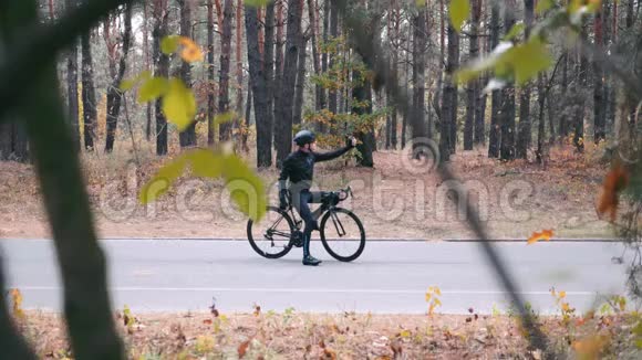 一位身穿黑色头盔的年轻职业自行车手正在打字把手机放进口袋开始骑在b路上视频的预览图