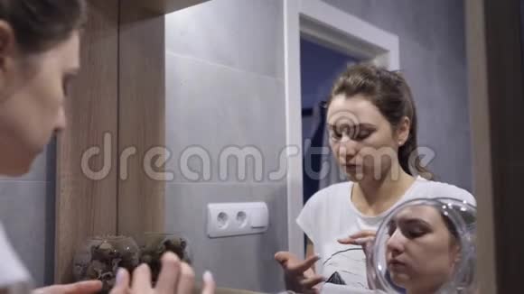 清洁面部的泡沫一个皮肤清洁的女孩用泡沫将面霜涂在脸上看着倒影视频的预览图