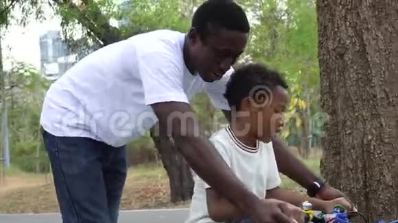 微笑快乐的非裔美国人父亲帮助他的儿子在公园里学习骑自行车视频的预览图