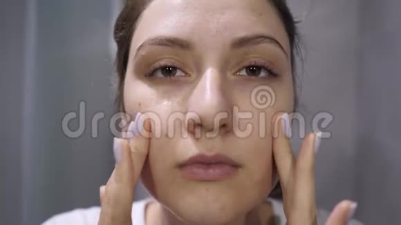 用泡沫洗脸一个漂亮的女孩看着镜头浴室里的特写女性肖像视频的预览图