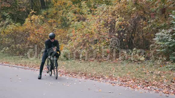 有吸引力的专业男性自行车运动员骑自行车服装与道路自行车站在秋季城市公园和打字邮件智能手机M视频的预览图