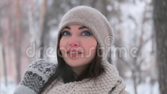 一个戴着深色头发的帽子的漂亮女孩在冬天站在雪地里的公园的肖像微笑着可爱视频的预览图