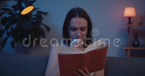 年轻沮丧的女人坐在沙发上读着非常悲伤的书情感女孩在书中的情节和情节中担心戏剧时刻视频的预览图