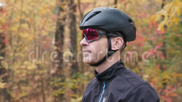 年轻帅气的职业男子自行车运动员在秋季公园骑自行车锻炼后脱下自行车器材迷人的白种人视频的预览图