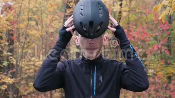 在秋季公园一个穿着黑色运动服的年轻迷人的白人男子戴上黑色自行车头盔和运动眼镜米视频的预览图
