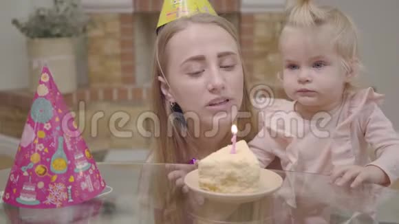 戴着派对帽的年轻白人妇女和小女婴在蛋糕上吹蜡烛的特写镜头可爱的孩子视频的预览图