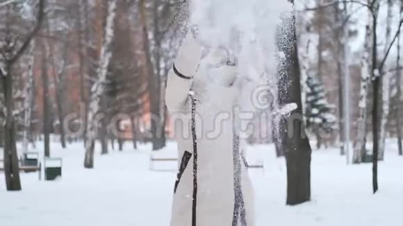冬天的森林里一个头发乌黑的美丽的年轻女子用手套举起双手雪在旋转微笑着视频的预览图